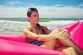 A young lady on a pink air raft near the water on the beach on a